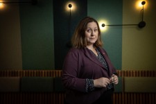  A woman in a dark suit stands in front of a wall